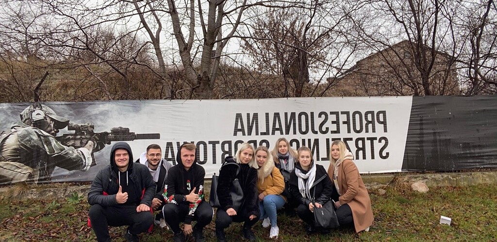 Grupa zadowolonych studentów pozuje do zdjęcia, w tle duży szyld Profesjonalne strzelnictwo